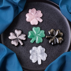 Five assorted natural crystal four-leaf clovers displayed on a decorative dark plate