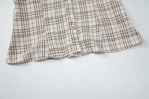 Detailed close-up of brown and white checkered shirt fabric with buttons and smooth stitching