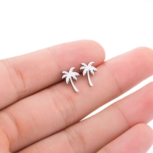 Macro shot of small silver coconut tree stud earrings held on a fingertip for size