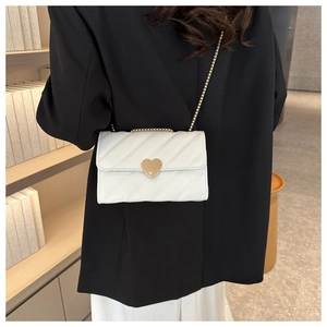 Detail of white quilted crossbody bag featuring a gold heart clasp and chain strap