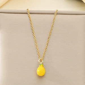 Detail view of gold titanium pineapple pendant with green leaves on a beige fabric background