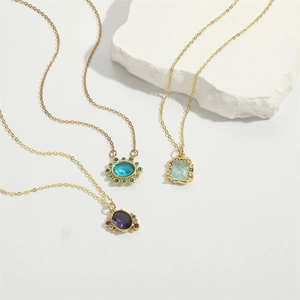 Minimalist gold necklaces with oval purple, blue, and green birthstone pendants on stone