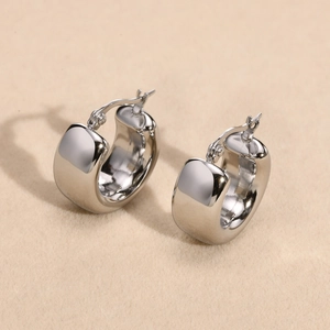 Detailed close-up of wide silver stainless steel hoop earrings on beige fabric background