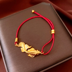 Macro detail of a vintage golden koi fish pendant on a red braided bracelet strap