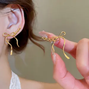 Elegant gold bow pendant earrings with polished ribbon design on a warm beige background