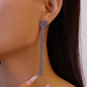 Detailed close-up of long purple tassel earrings with heart-shaped crystal studs on a model