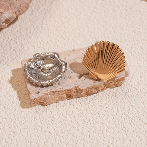 Detail of gold and silver shell ear cuffs on stone base showing metallic texture and clip-on back