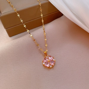 Detailed close-up of a gold clover necklace with pink crystals on soft beige fabric