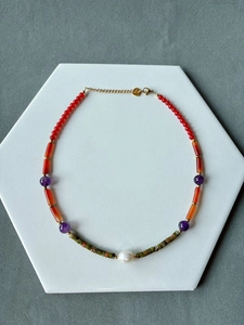 Detail of bohemian colorful beaded necklace with green stone, red tubes, and white pearl
