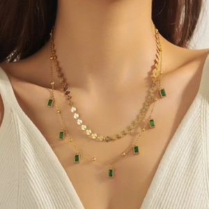 Close-up of double-layer gold necklace with green emerald-cut stones on a model
