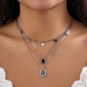 Macro shot of silver layered necklace featuring black teardrop gem and coin pendants