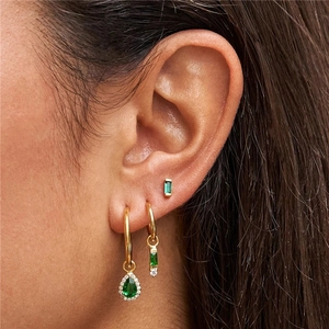 Golden earrings set with emerald green gems and rectangle drop charms on female model