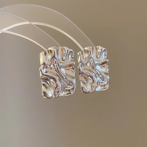 Detailed view of silver square crumpled earrings with a liquid metal texture on a stand