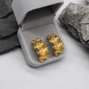 Detailed close-up of golden irregular wrinkled earrings inside a grey velvet jewelry box