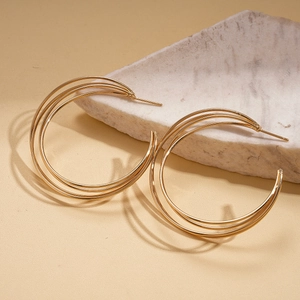 Close-up of triple-layered golden geometric hoop earrings on a neutral stone surface