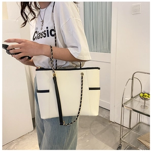 Detail of a chic cream tote bag featuring black piping and an elegant gold chain strap