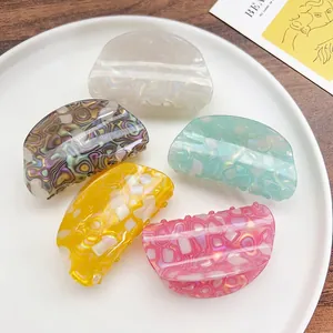 Five colorful marble acetate hair claws in pastel tones on a white ceramic plate