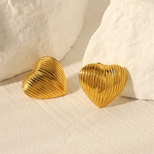 Macro detail of gold-plated heart earrings featuring vertical pleated texture on stone background