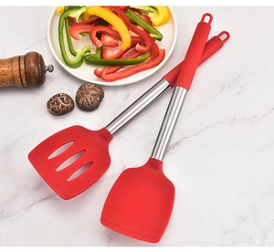 Detail of red silicone spatula and slotted turner with metal handles on marble background