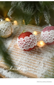 Close-up of 8cm glittery Christmas ball with white lace detail on snowy wood