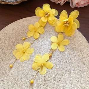 Detail of yellow fabric floral tassel earrings featuring gold beads on a matte tray