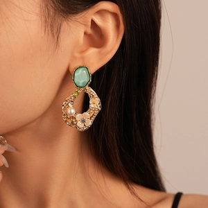Macro detail of vintage gold floral earrings with green gemstone and pearl accents