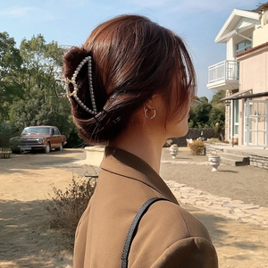 Elegant gold metal shark hair claw clip with pearls shown on a woman in an outdoor setting