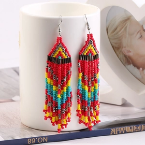 Macro detail of colorful beaded tassel earrings with geometric patterns on a ceramic cup