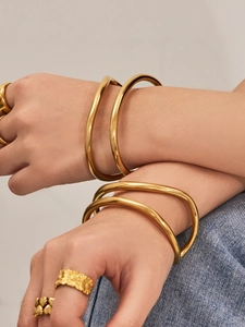 Dettaglio ravvicinato di un bracciale a C placcato oro 18k e anelli a strati sulla mano