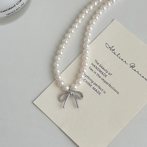 Elegant pearl necklace with a central silver bow pendant on a textured grey background