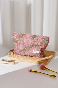 Detailed view of pink daisy embroidery on green fabric makeup bag with white logo label