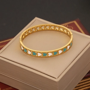 Vintage gold stainless steel bangle with white and teal heart patterns on a display box