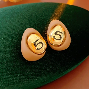 Close-up of vintage egg-shaped gold plated earrings with beige enamel and number five