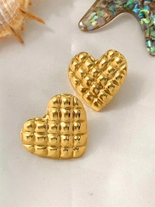 Macro view of gold heart stud earrings with quilted texture on white silk background