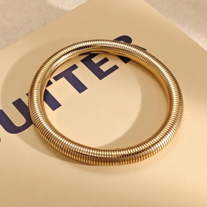 Vue macro montrant la texture détaillée et la structure métallique flexible Tubogas dorée du bracelet