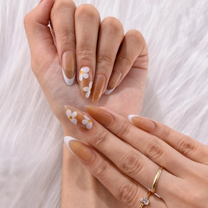 Detail of almond French press-on nails with white daisies and gold foil accents