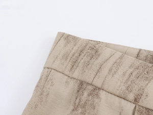 Dettaglio dei pantaloni beige con trama marrone che mostra cuciture in vita e pieghe