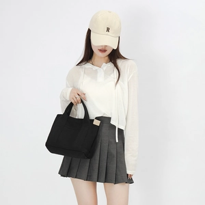 Detail of black canvas tote bag with contrast cream side label and durable top handles
