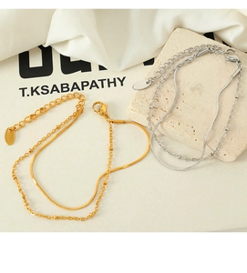 Detail of layered gold and silver snake chains with bead accents on stone surface