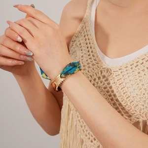 Detailed view of matte gold metal buckle and blue floral fabric on a stylish cuff bracelet