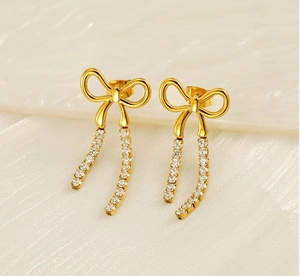Close-up of golden bow earrings with sparkling rhinestone tassels on white texture