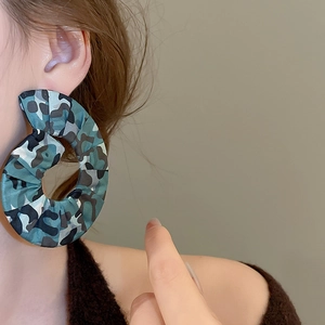 Detail of a large camouflage fabric hoop earring worn by a model in a stylish side view