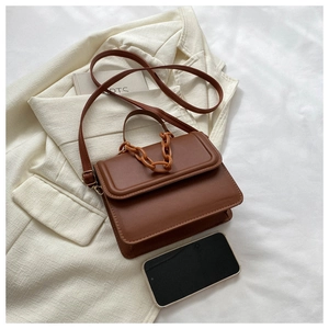 Detailed view of a brown faux leather crossbody bag with chain handle on a white blazer