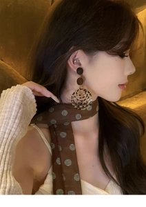 Detail of round leopard print resin earrings with deep brown and amber geometric design