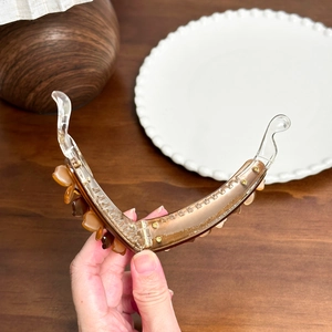 Elegant amber and transparent acetate banana hair clip held in hand for styling