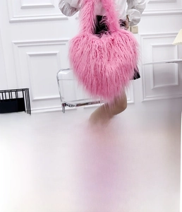 Detail view of pink heart-shaped sheep fur crossbody bag worn on shoulder by model