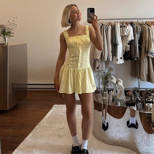 Detail view of yellow strap dress with button decor, ruched chest and ruffle hemline