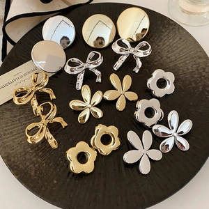 Gros plan de boucles d'oreilles nœuds et fleurs en métal doré et argenté sur plateau