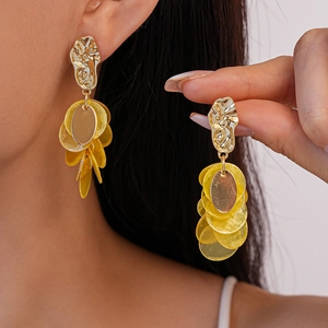Macro shot of geometric shell earrings with gold textured plates and yellow pendants