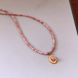 Detail view of pink rhodochrosite beads and gold oval pendant on a luxury necklace